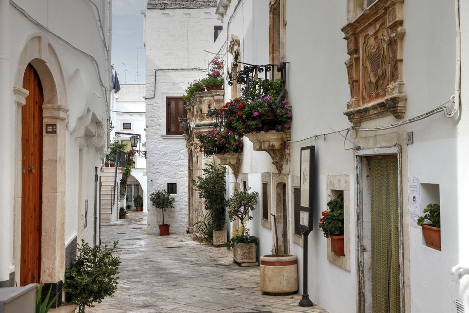 Picturesque alley with white buildings and flowers in Locorotondo, Italy.
