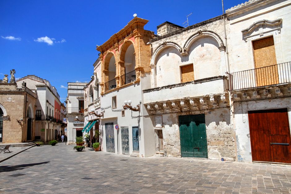 Historic buildings line a sunny street in a picturesque Italian town center.