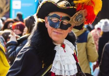 A vibrant scene of a costumed attendee at the Venice Carnival showcasing traditional Venetian attire with colorful feathers.