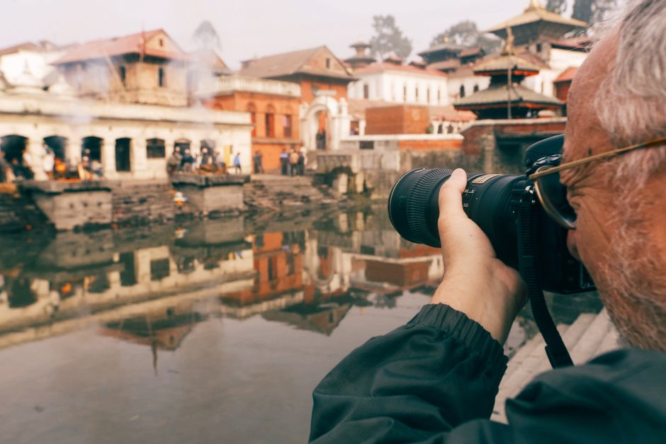 A senior photographer captures a historic temple landscape by the water.
