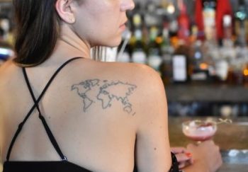 Woman in floral kimono at a bar, showcasing a world map tattoo on her back.