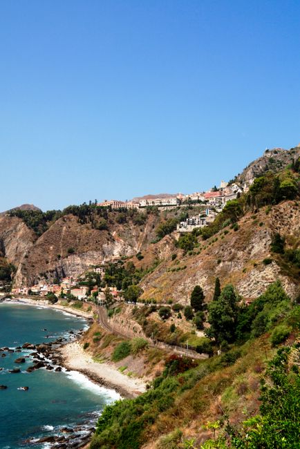 Beautiful aerial view of Taormina's coastline with clear blue sky and rocky landscape in Sicily, Italy.
