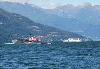 Two boats cruise across Lake Como with mountainous backdrop under clear blue skies.