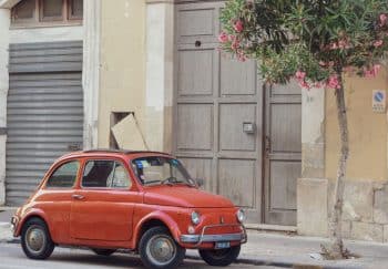 Charming vintage Fiat 500 parked beside blooming trees on a Sicilian street, capturing urban nostalgia.