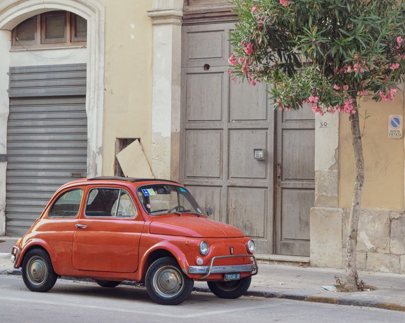 Charming vintage Fiat 500 parked beside blooming trees on a Sicilian street, capturing urban nostalgia.