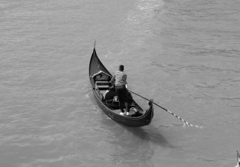 Black and white image of a gondolier steering a traditional gondola on a Venetian canal.