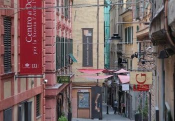 Explore the quaint narrow alleyway in Genoa's historic district, showcasing colorful buildings and vibrant local culture.