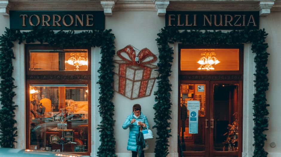Woman in a blue jacket outside Torrone shop in L'Aquila, Italy during winter.