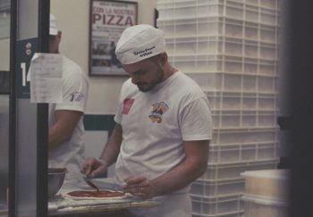 Pizza chef spreading sauce on dough in Napoli restaurant kitchen.