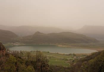 Capture of Kalterer See during a misty dawn, showcasing tranquil lake and mountain landscape.