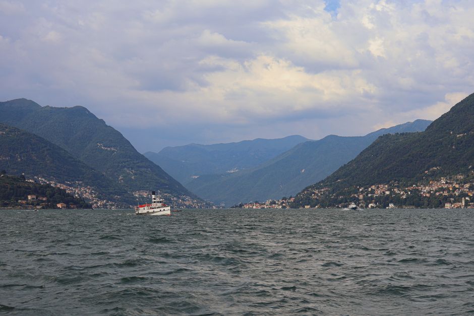 Boat cruising on Lake Como with mountains and cloudy sky in the background.