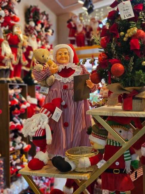Vibrant Christmas store display featuring Mrs. Claus with teddy bear, surrounded by festive decor.