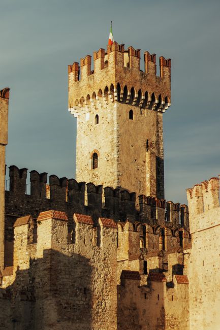 Close-up of a medieval castle tower with detailed stonework and battlements, clear sky in the background.