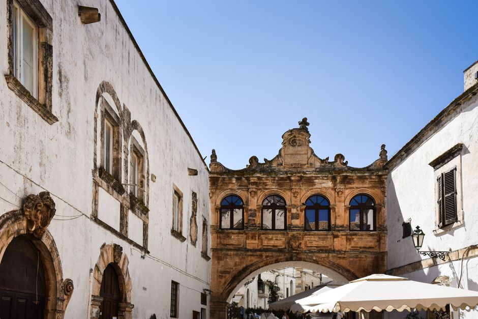 Scenic view of a historic archway and white buildings in Ostuni, Apulia, Italy under a clear blue sky.