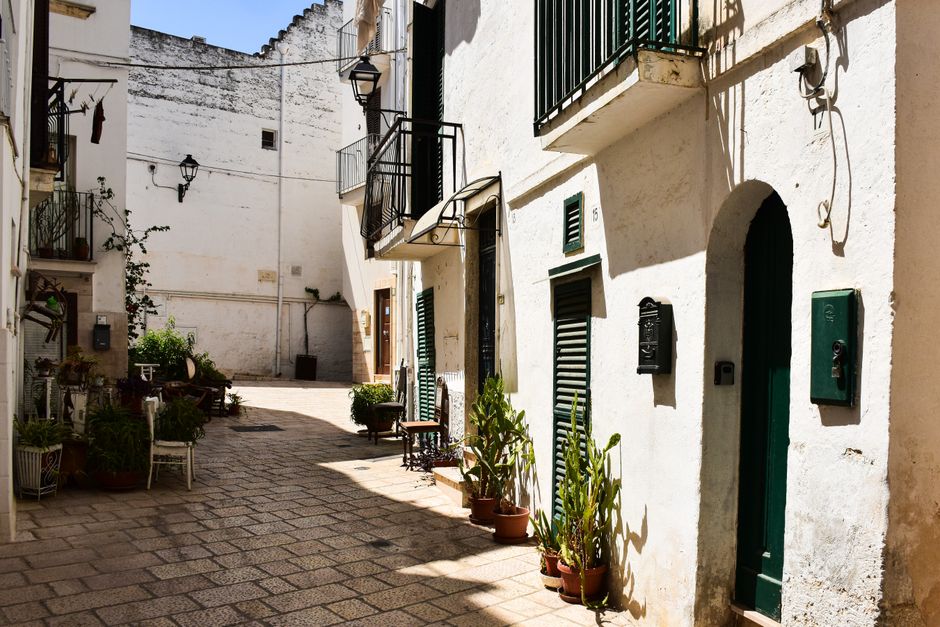 Sunlit alleyway in a classic Puglian town with whitewashed buildings and plants.