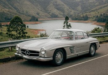Vintage car parked by a stunning mountain lake with lush greenery in the background.
