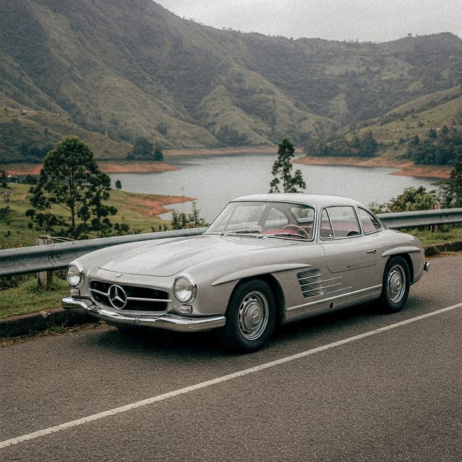 Vintage car parked by a stunning mountain lake with lush greenery in the background.
