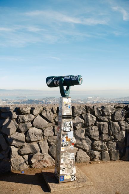 Public telescope with stickers overlooking Los Angeles skyline.
