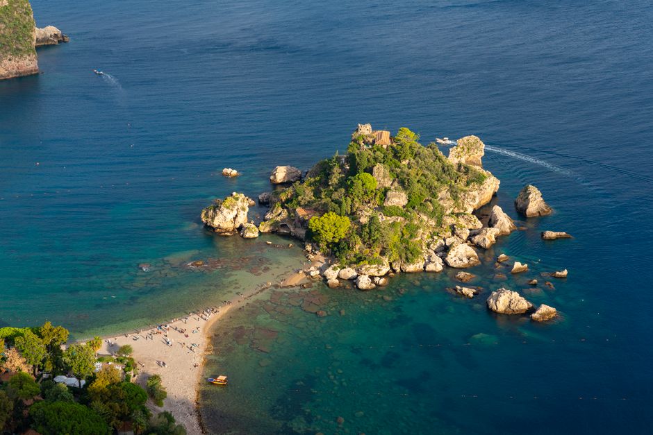 A breathtaking aerial shot of Isola Bella in Sicily, Italy, showcasing its vibrant greenery and crystal-clear blue waters.