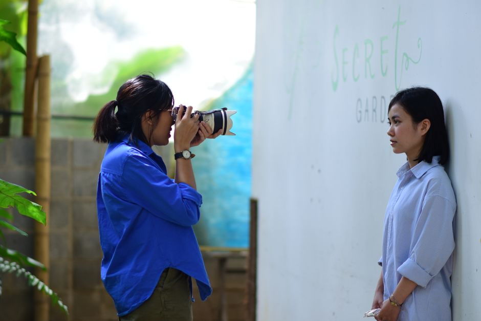 A female photographer takes a portrait photo of a young woman outdoors in a secret garden.