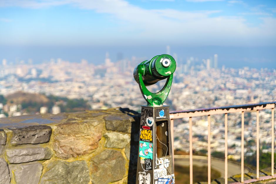 A green coin-operated telescope with a city view of San Francisco in the background.
