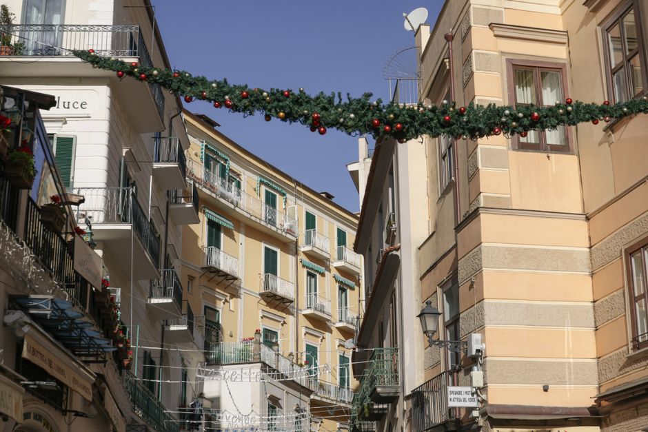 A vibrant Italian street adorned with festive decorations under a clear blue sky.