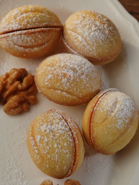 Close-up of walnut shaped pastry cookies sprinkled with powdered sugar on a white plate. Perfect for dessert lovers.