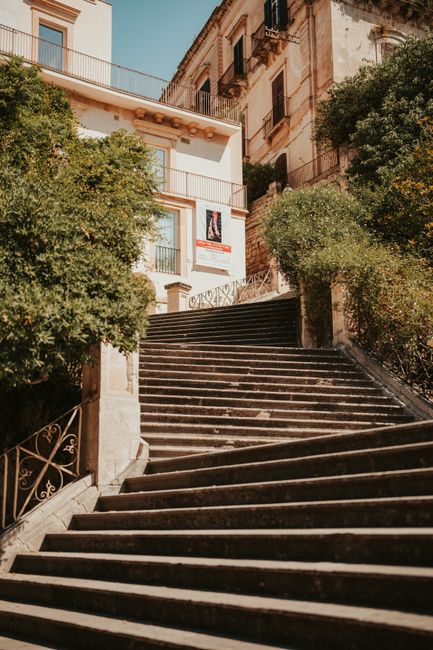 Charming stone staircase in Modica, Sicily, Italy surrounded by lush greenery under a bright blue sky.