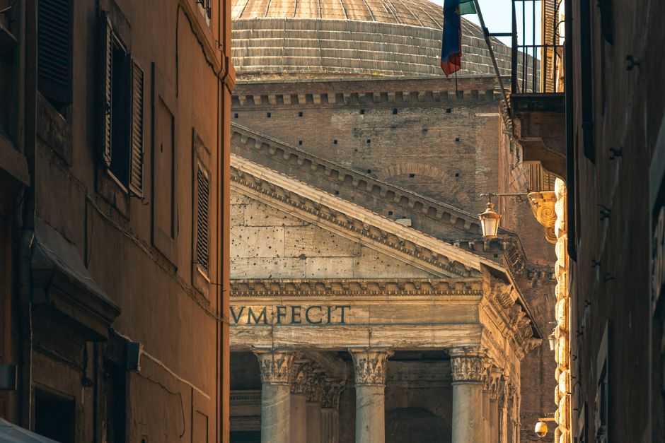Classic view of the Pantheon entrance framed by narrow Roman alleyways at dusk.