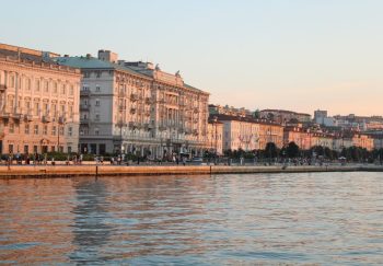Beautiful sunset over historic waterfront buildings in Trieste, Italy reflecting off the Adriatic Sea.