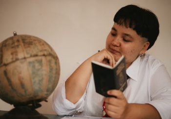 A pensive young adult reading a passport next to a vintage globe, symbolizing travel dreams.