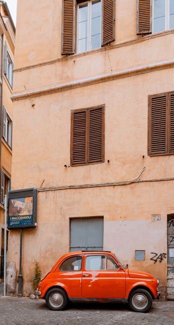 A classic red car parked beside a rustic building in a charming Roman street.