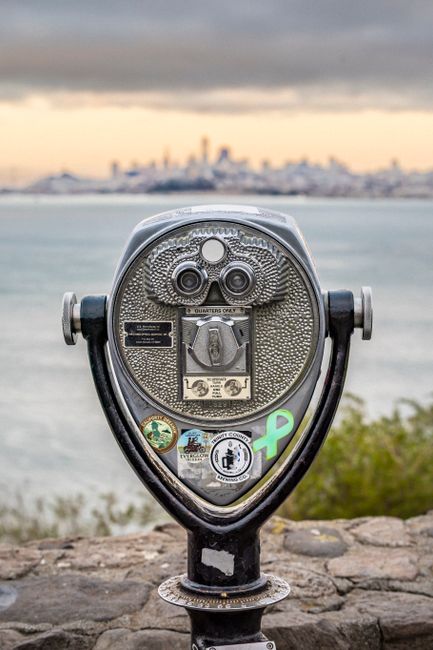 Coin operated binoculars with city skyline view during sunset, creating a striking silhouette.
