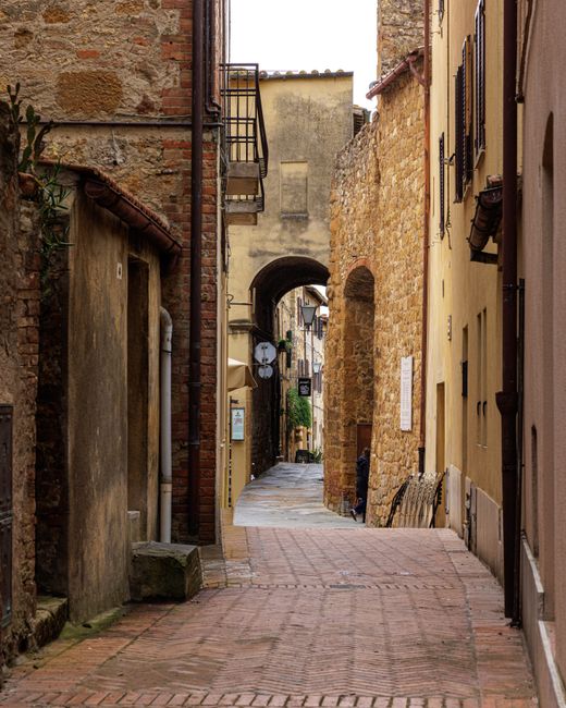 Explore a rustic narrow alley in Tuscany with historic stone architecture and warm tones.