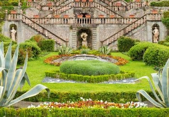 Stunning Italian garden featuring lush greenery, colorful flowers, and intricate stone sculptures.