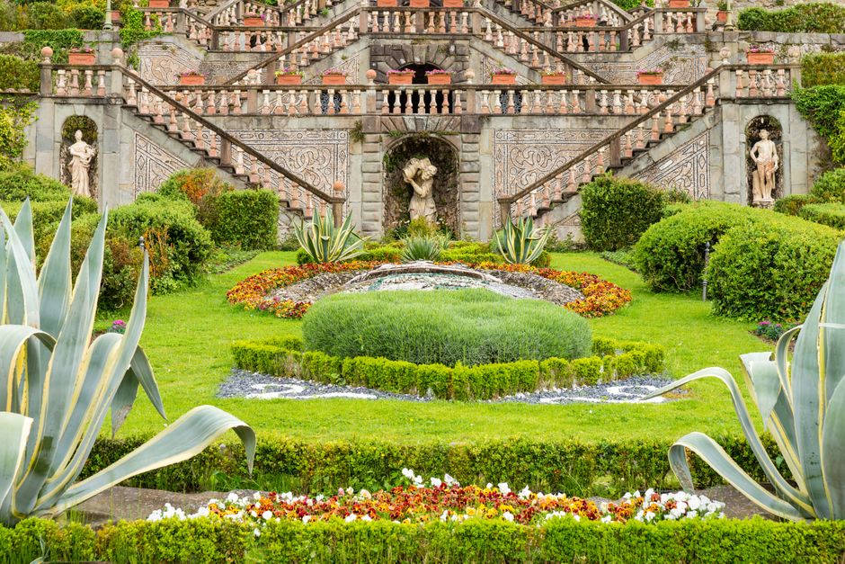 Stunning Italian garden featuring lush greenery, colorful flowers, and intricate stone sculptures.