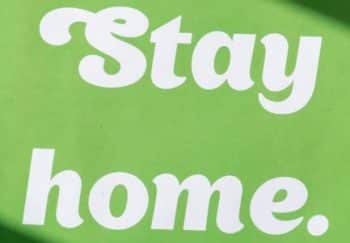 A green sign with the text 'Stay home.' promoting quarantine safety and social distancing.