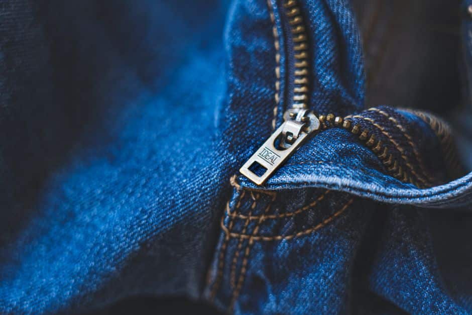 Close-up of blue denim fabric featuring a metal zipper with detailed stitching.