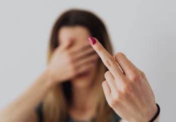 A woman indoors showing a bold gesture with her middle finger extended. Focus on hand.