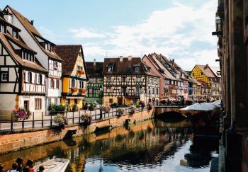 Exterior of old traditional half timbered houses located on embankment near canal flowing in Colmar on sunny day