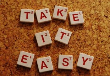Wooden Scrabble tiles spelling 'Take It Easy' on a cork surface in top view.