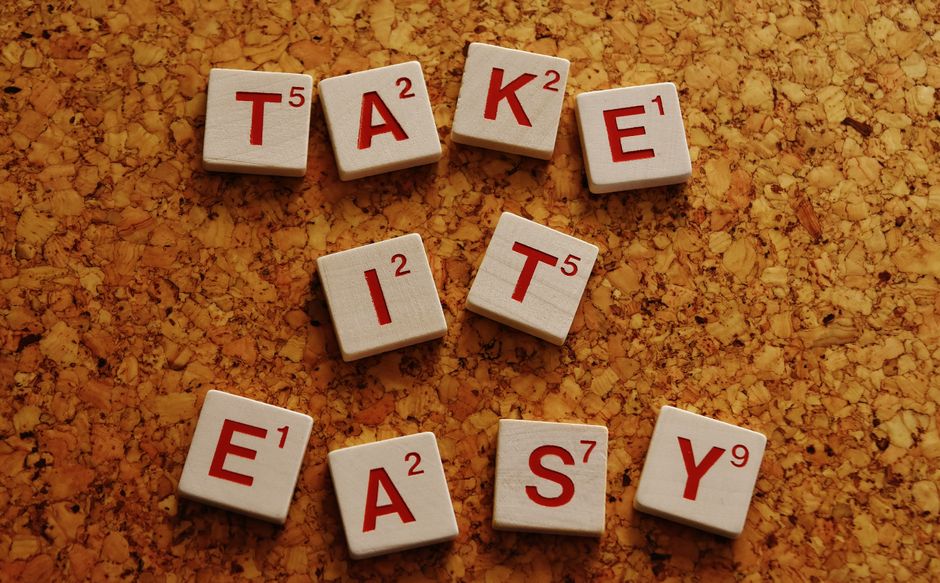 Wooden Scrabble tiles spelling 'Take It Easy' on a cork surface in top view.