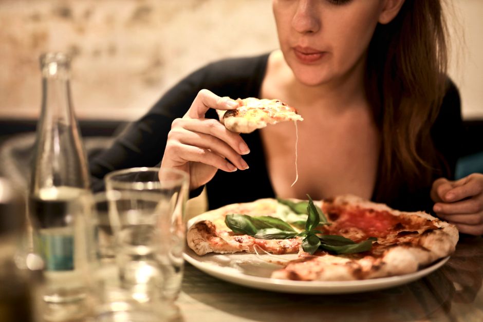 A woman savoring a delicious pizza slice in a cozy indoor restaurant setting.