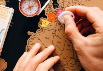 Close-up of hands scratching a travel map, featuring a compass and polaroid, symbolizing travel planning.
