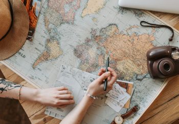 Top view of a woman's hands planning a trip with a map, camera, and travel items.