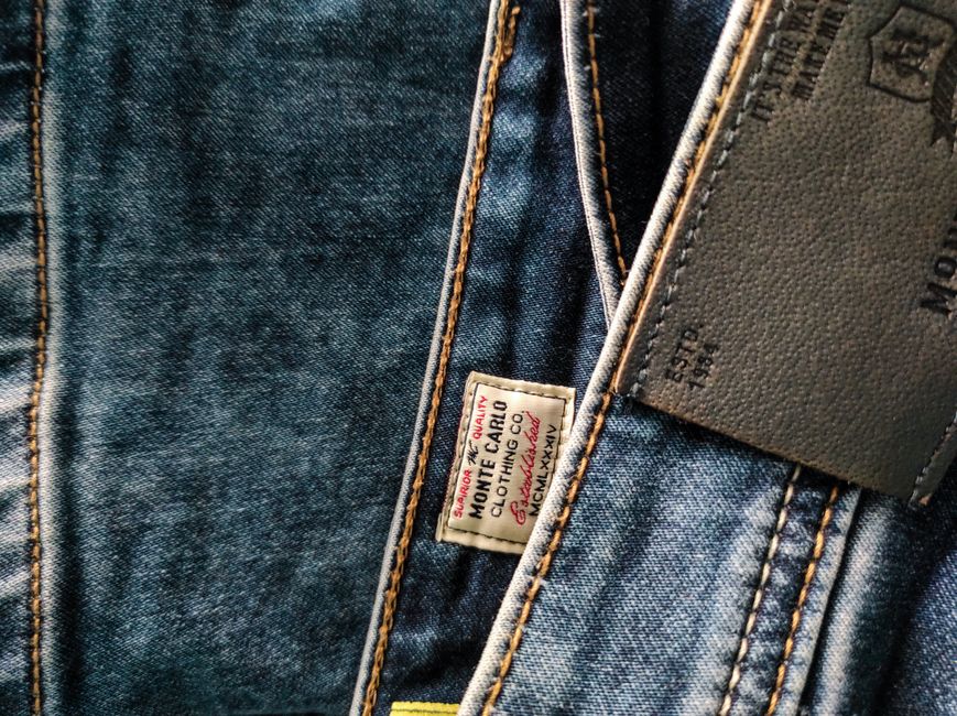 Detailed view of blue denim jeans showcasing stitching, leather patch, and brand label.