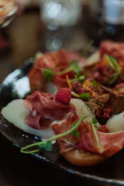 A beautifully arranged charcuterie plate featuring prosciutto, melon slices, and fresh raspberries.