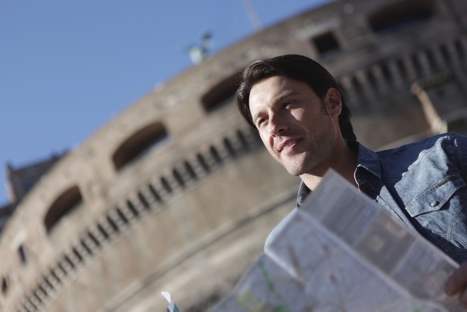 Man in denim jacket sightseeing near historical building, enjoying travel with map.