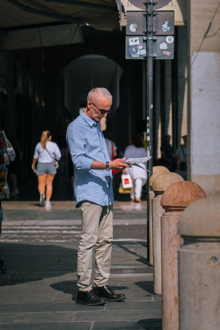 Elderly man reading a guide in a sunny city street, showcasing urban lifestyle.