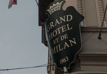 Street view of the iconic Grand Hotel et de Milan's facade with flags displayed prominently.